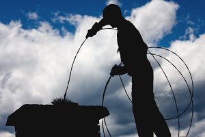 Manasquan chimney service includes cleaning as shown in this silhouette photo of a chimney sweep on a roof with a brush in the top of a chimney