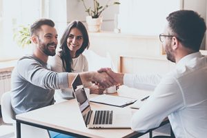Agent shaking hands with clients across a desk after securing Seaside Park rentals because they booked early