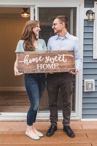 Happy couple holding a home sweet home sign after completing their journey searching homes for sale in Monmouth County NJ