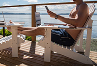 Person on laptop and cellphone sitting on a deck overlooking the ocean